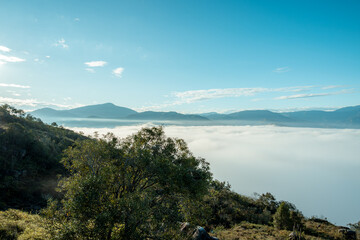 Sky meeting earth with thick white fog filling the valley, green hillsides and distant mountain ranges emerging above the morning cloud blanket