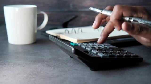 Person using calculator while holding pen during accounting work on stone desk with white coffee mug