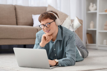 Young man in headphones working with laptop on carpet at home