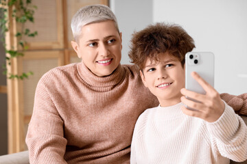 Fototapeta premium Mother and her teenage son in warm sweaters taking selfie on sofa at home