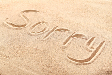 Word SORRY written on sand, closeup