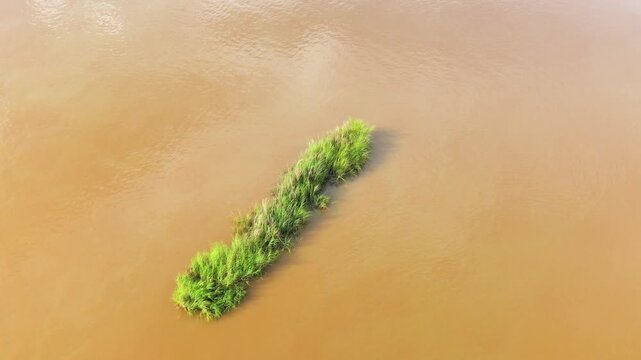 A small patch of green grass grows on an isolated island in the middle of a muddy river, seen from above in Luang Prabang, Laos.