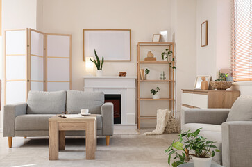 Fototapeta premium Interior of light living room with grey sofas, fireplace and bookshelf