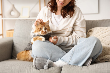 Woman in soft slippers with cute cat on sofa at home