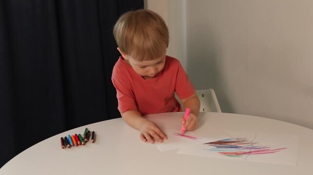 A preschool-aged boy draws lines with a pencil, making strokes on a white sheet of paper. The boy scribbles on the paper.