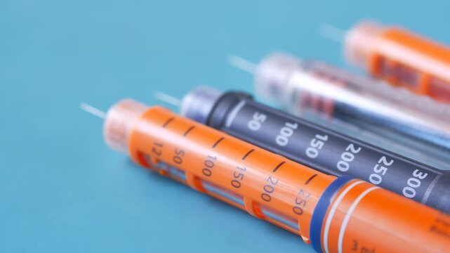 Close-up of a row of colorful insulin pens for diabetes treatment, showing different dosage numbers, on a light blue background