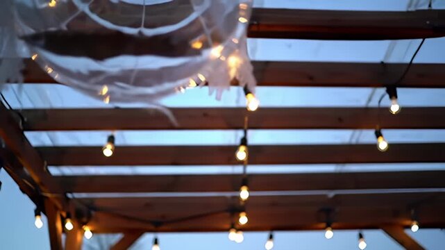 Wooden pergola strung with lights under a blue sky, out of focus and indistinct