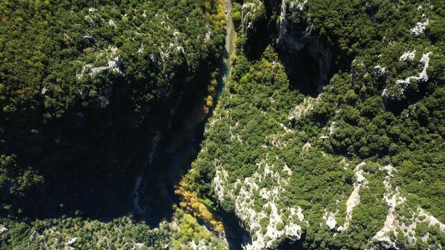 Stunning aerial view of dense green forest and rocky cliffs in Vikos Aoos National Park, Greece, with a river cutting through the landscape.