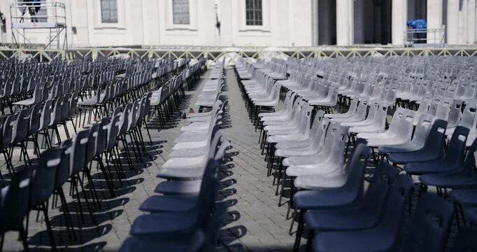 Cinematic establishing shot of empty row of chairs at Saint Peter square in Vatican as preparation for Eastern holiday ceremony on spring sunny day, selective focus