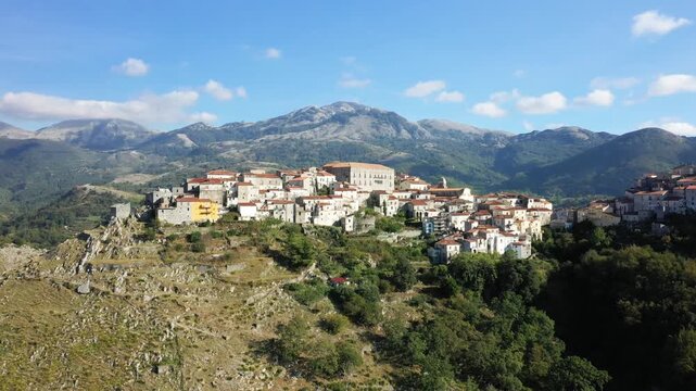 Scenic aerial view of the historic hilltop village of Aieta surrounded by lush mountains under a clear blue sky. Picturesque Mediterranean architecture with terracotta rooftops nestled in the Italian