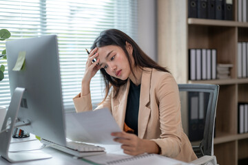 Fototapeta premium Stressed asian businesswoman having headache while reading documents at office desk
