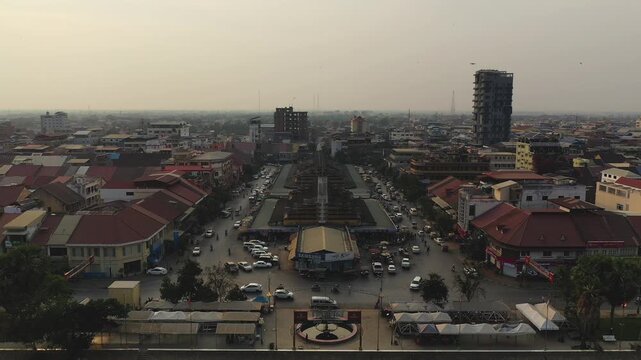 Wide aerial shot of the central market district in Battambang, Cambodia, featuring busy streets, urban buildings, and a hazy sky.