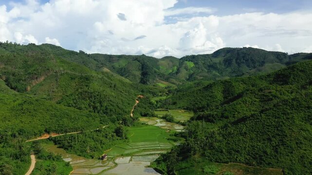 Aerial view of vibrant green hills and terraced rice fields in the countryside near Nong Khiaw, Laos, under a bright sky. Scenic rural landscape with natural beauty and agricultural patterns.