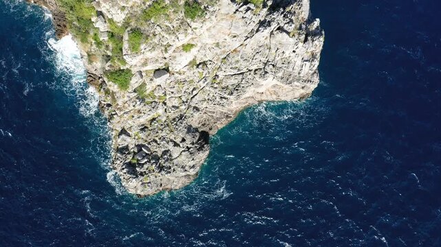 Aerial view of a rugged rocky cliff jutting into deep blue ocean waters along the Capo di Conca coastline. Vibrant natural textures and dramatic seascape create a striking coastal scene.
