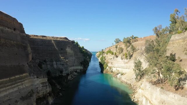 A stunning view of the Corinth Canal cutting through rocky cliffs with clear blue water and a bright sky, located in Greece.