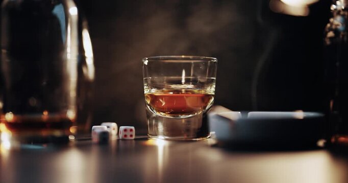 Gambling macro scene. A glass of whiskey alcohol drink, a bottle, smoke of cigar dice on black