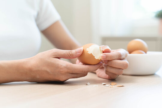 Close-up shot of woman hands peeling shell of boiled egg on the table.