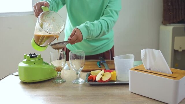 Person pouring freshly blended fruit juice through strainer into glass