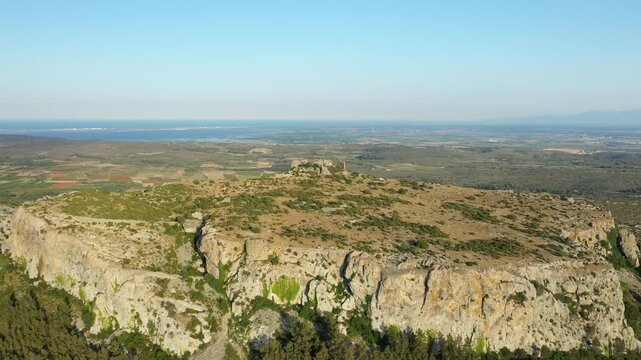Wide aerial shot of the rugged landscape surrounding Chateau de Opoul Perillos in southern France, with distant fields and coastline visible under a clear sky.