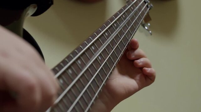 A detailed close-up shot of a young musician's hands playing the fretboard of a four-string electric bass guitar. The person practices fingering techniques and plays notes. Music lesson concept.