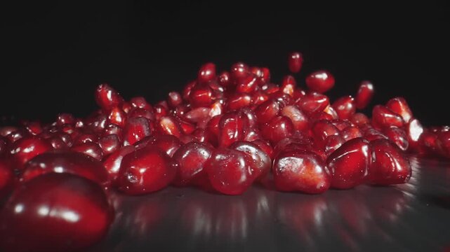 Ripe pomegranate fruit grains falling and bouncing on black surface with reflection in slow motion