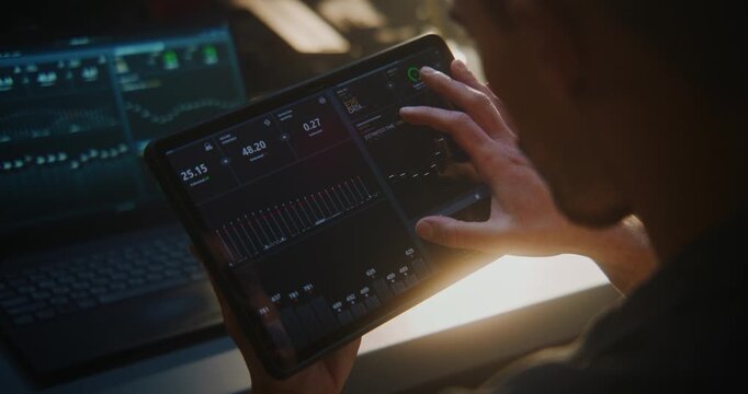 Auto Technician Using Tablet For Engine Diagnostics in Workshop. With Laptop Connected Vehicle, Man Monitors Performance Charts and System Data. Digital Automotive Service and High Tech Maintenance.