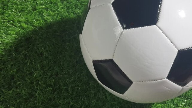 Football ball rolling across natural grass and stopping near the edge of the frame, highlighting outdoor sport equipment and football field atmosphere.