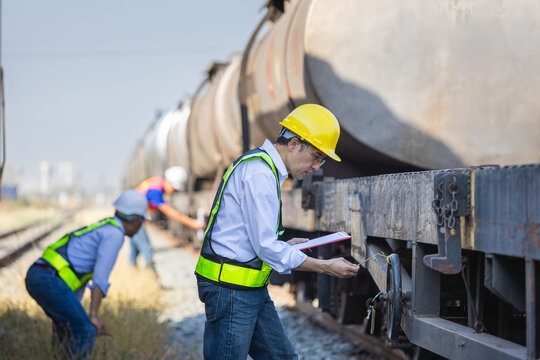 Railway inspector checking safety seals and valves on freight train wagons, Engineering team performing routine maintenance on industrial train cars, Supervisor with clipboard verifying cargo shipment