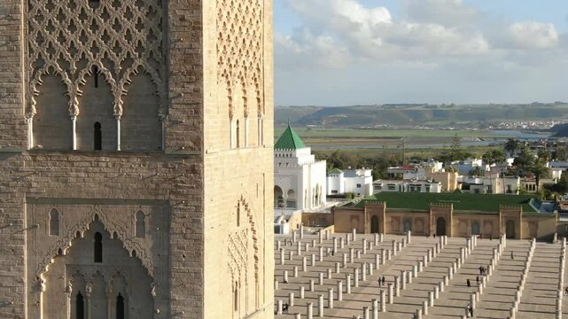 Detailed close-up of the iconic Hassan Tower in Rabat, Morocco. Showcases the intricate Almohad-style stone carvings and arched windows, with the historical pillars and river in the background. Ide