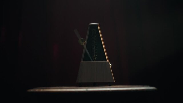 A close-up shot of a classic mechanical metronome ticking on a dark wooden surface. The camera performs a smooth dolly-in move toward the swinging pendulum, followed by a dolly-out. Moody red lighting