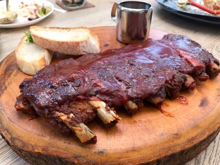 Grilled pork baby back ribs smothered in barbecue sauce served on a wooden cutting board with toasted bread slices