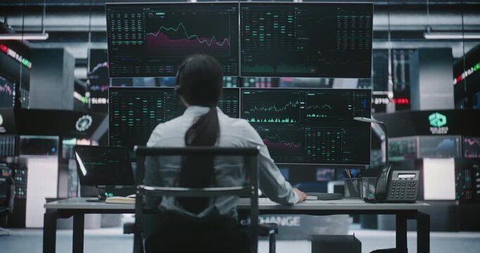 Focused Asian Woman Trader Leans Over Digital Tablet Verify Financial Data While Sitting in Front of Four Large Monitors. Concept of Cross Platform Analysis and Meticulous Precision in Stock Exchange.