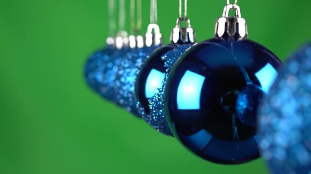 Shiny blue Christmas ornaments hang in a row against a vibrant green background.