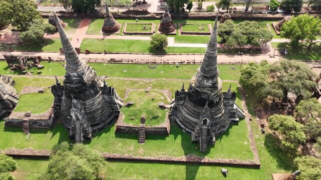 Dron shot flying along the shaded side of historic ruins at Wat Phra Si Sanphet temple, Thailand.