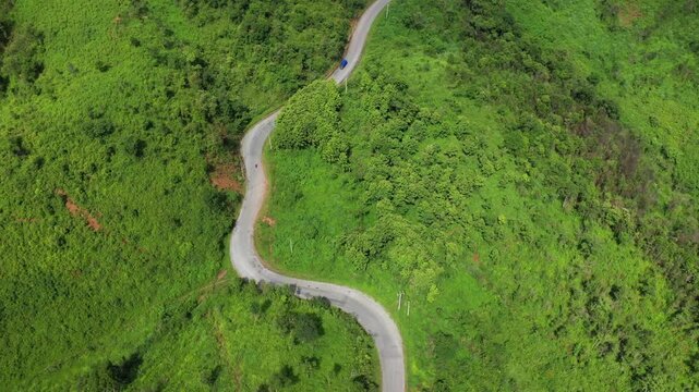 Aerial view of a curvy road winding through lush green hills in the countryside between Phonsavan and Phou Khoun, Laos. The vibrant landscape highlights the natural beauty and remote atmosphere of the
