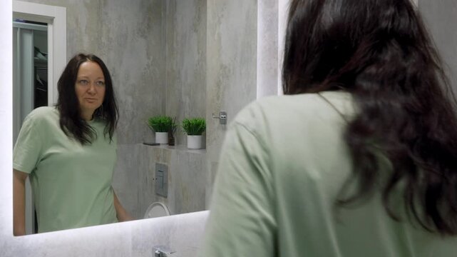 A woman's mood changes from happy dancing to sadness while looking at her reflection in a bathroom mirror. Explores self-esteem, body image, and emotional instability.
