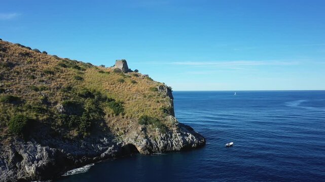 Scenic view of the rugged Capo Palinuro coastline with clear blue sea and a small boat near the cliffs under a bright sky.