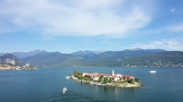 Aerial view of Isola dei Pescatori, a picturesque island with traditional buildings and a church, surrounded by Lake Maggiore and mountain scenery in Italy.