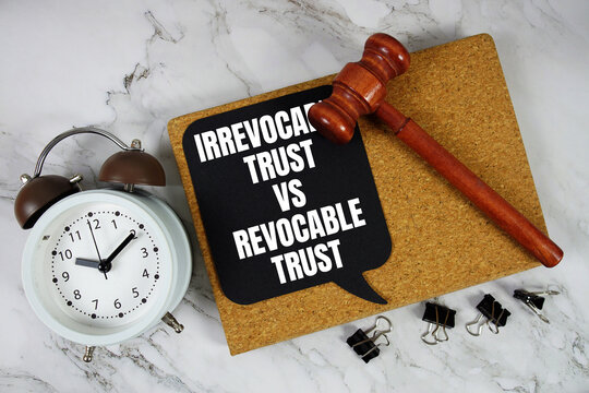 Irrevocable Trust vs Revocable Trust text on speech bubble with alarm clock and wooden gavel on marble background