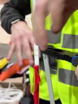 Man in high visibility vest using crimping tool to secure electrical wires with red plastic plugs for installation process
