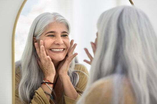 Happy Latina woman touch her refreshed skin with fingers after treatment or cosmology procedure, smile, feel satisfied with shiny, silky condition of skin. Aesthetic medicine, anti-ageing, self-care