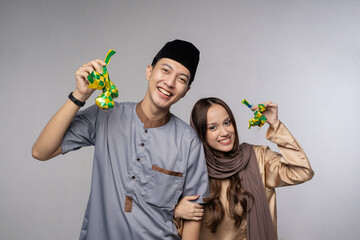 Fototapeta premium Smiling malay couple holding green envelopes in studio portrait wearing hijab and songkok, joyful giftgiving for eid celebration,