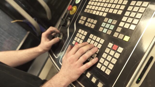 Machine operator adjusts settings on a CNC control panel using keypad and rotary selector. Industrial production control inside a manufacturing facility.