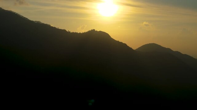 4K brilliant golden sunrise glowing brightly behind dark silhouetted mountain ridges