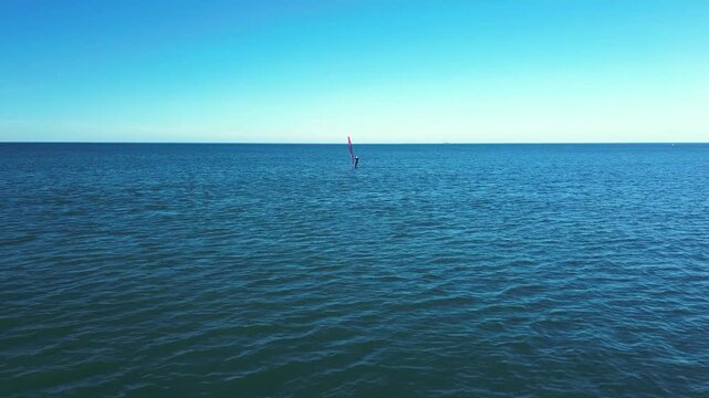 coastal drone shot capturing a windsurfer riding the waves in front of the historic Mulberry Harbour in Asnelles, symbolizing freedom and heritage.