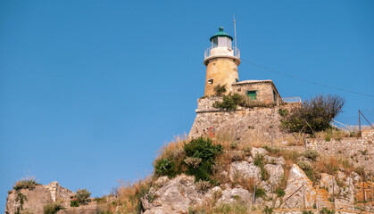 Corfu Old Fortress lighthouse on a rocky hill in Old Town, Greece. Weathered stone walls, blue sky, Low angle view