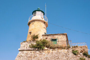 Corfu Old Fortress lighthouse on a rocky hill in Old Town, Greece. Weathered stone walls, blue sky, Low angle view