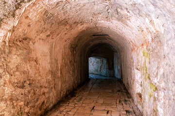Stone tunnel passage inside the Old Fortress in Corfu Old Town, Greece. A bright exit over cobblestone path