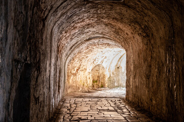 Stone tunnel passage inside the Old Fortress in Corfu Old Town, Greece. A bright exit over cobblestone path