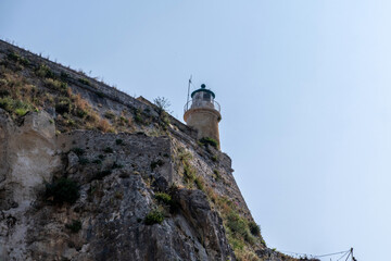Corfu Old Fortress lighthouse on a rocky hill in Old Town, Greece. Weathered stone walls, blue sky, Low angle view